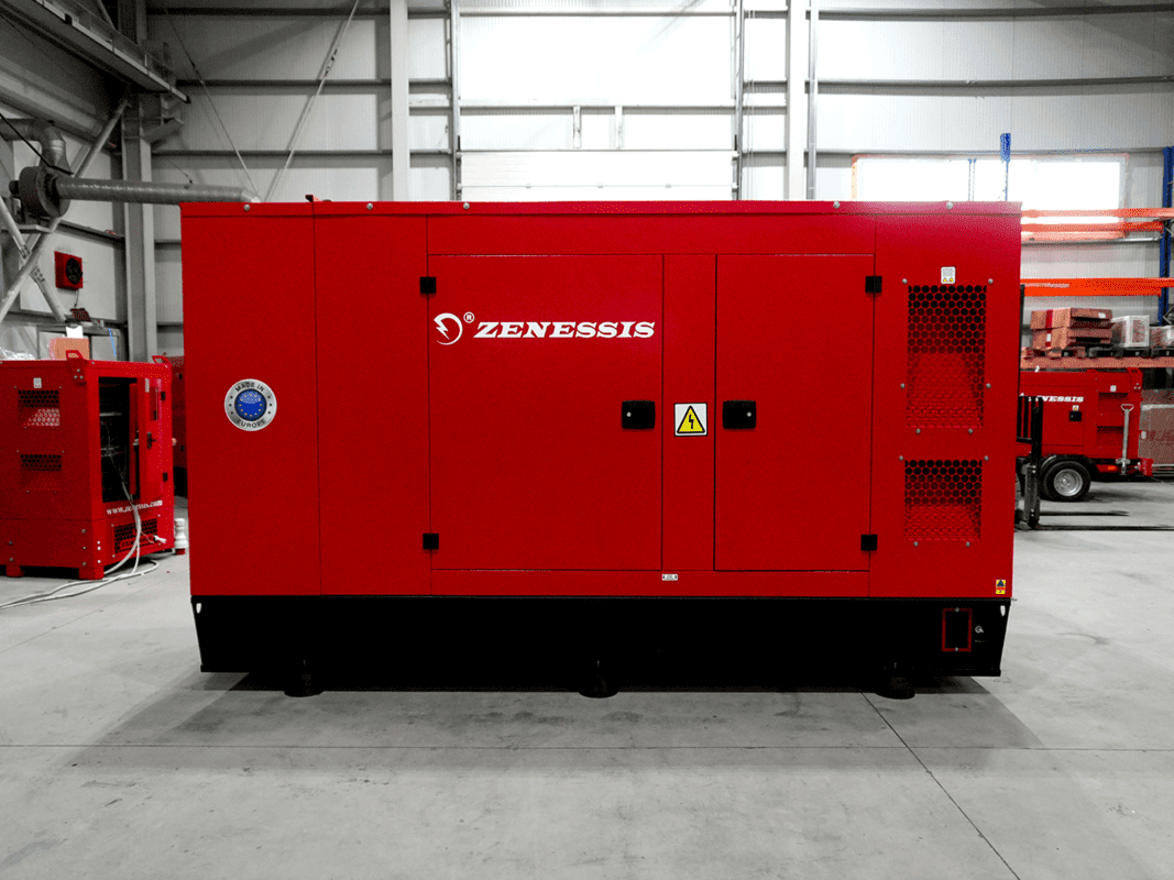 A red Zenessis generator inside a warehouse. The generator features the Zenessis logo on the side, with ventilation grilles and a 'Made in Europe' label visible. The surrounding environment has a high-ceiling warehouse with other equipment in the background.