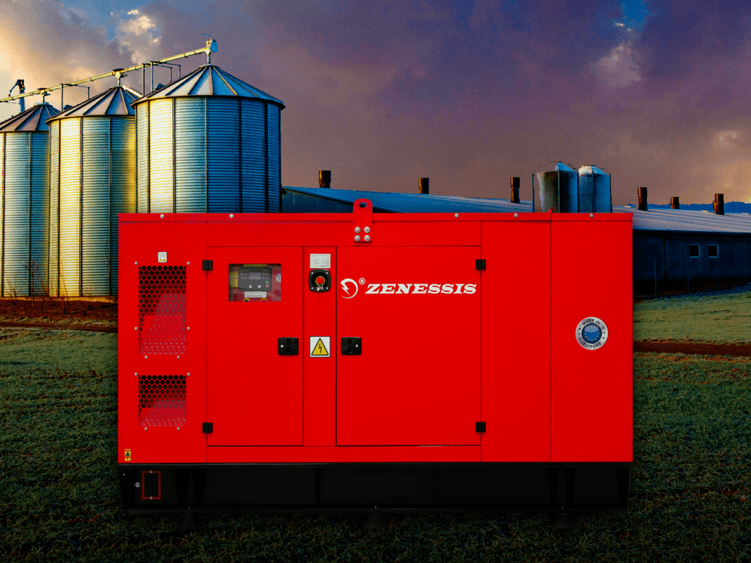 A red Zenessis generator in an agricultural setting, positioned in front of large metal silos at a farm. The generator's control panel is visible on the side, and the ‘Made in Europe’ logo is displayed. The background shows a field with a barn and silo structures under a colourful sky.